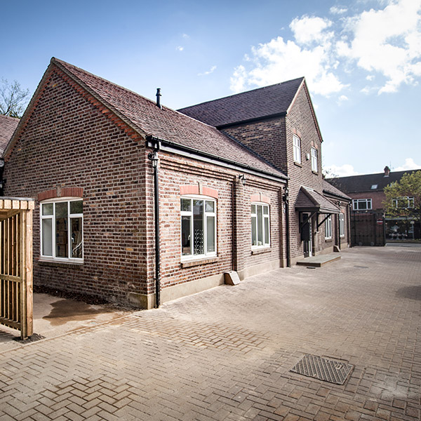 The Coach House from the yard: a long low red-brick range under two pitched slate roofs, white casement windows, a timber gate and a block-paved courtyard.